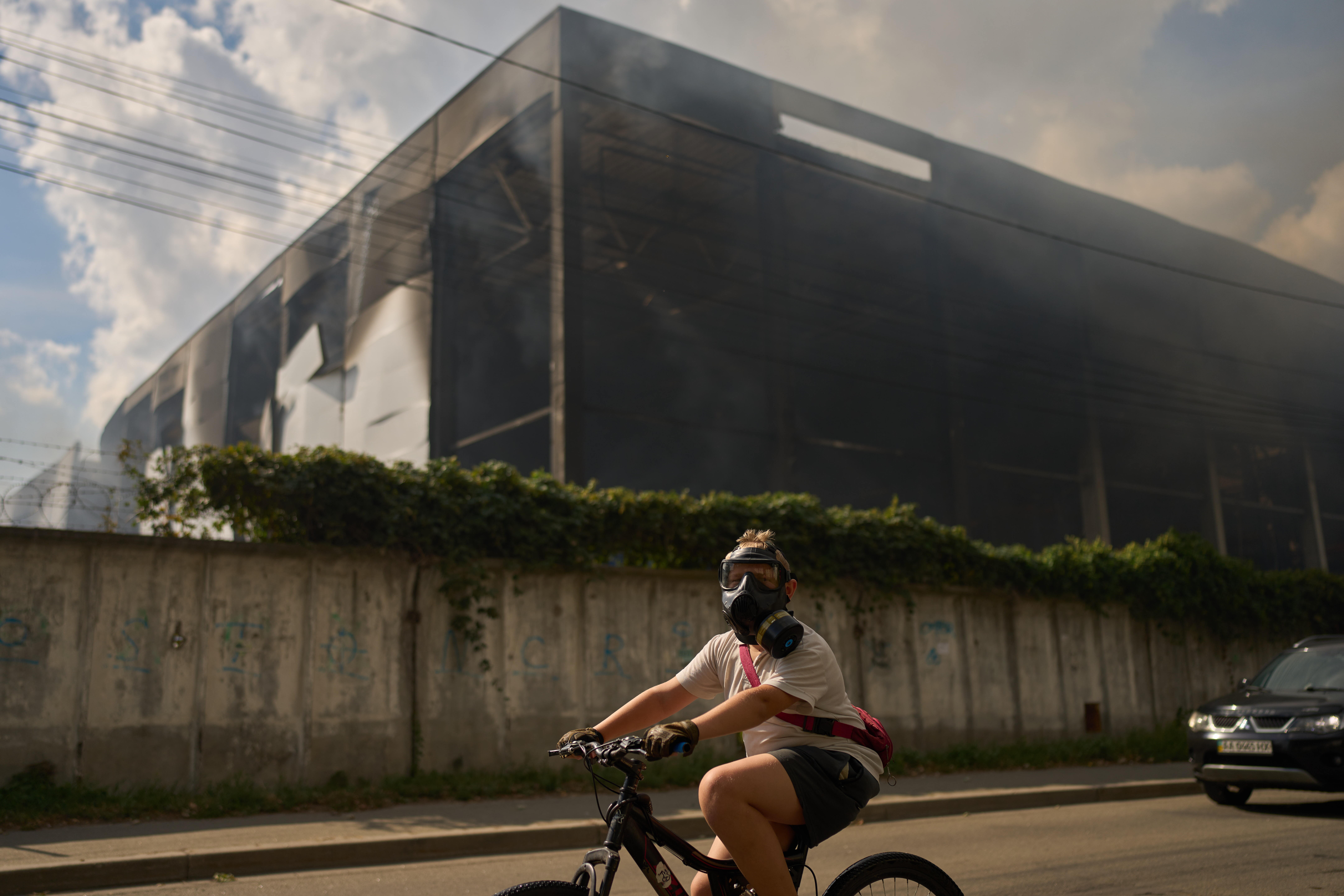 A local resident wears a gas mask as he rides a bicycle past a partially destroyed warehouse after a Russian drone attack in Brovary on the outskirts of Kyiv, Ukraine, Friday, Sept. 4, 2026.